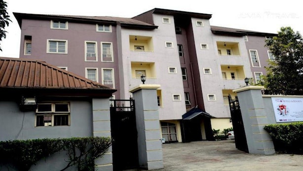 A multi-story hotel with a central entrance, a gated driveway, and a signboard. - Room-christine Apartments-guest Room (Port Harcourt)
