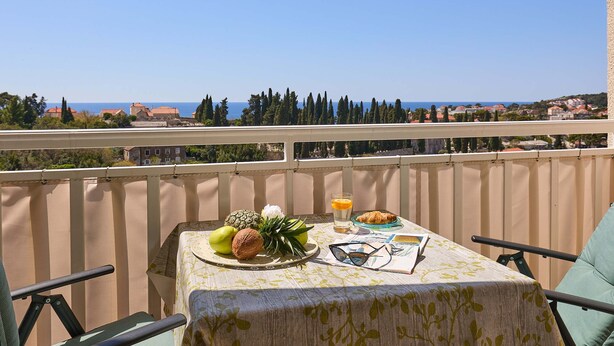 A balcony with a table set for breakfast, overlooking a coastal view. - Apartment Terra (Dubrovnik)