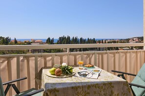 A balcony with a table set for breakfast, overlooking a coastal view. - Apartment Terra (Dubrovnik)