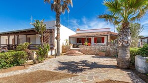 A courtyard with stone flooring, palm trees, and a building with a tiled roof and red accents. - 1907 Villa Alma (Alliste)