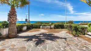 A paved pathway leading to a scenic view of the sea, with palm trees and a clear sky. - 1907 Villa Alma (Alliste)