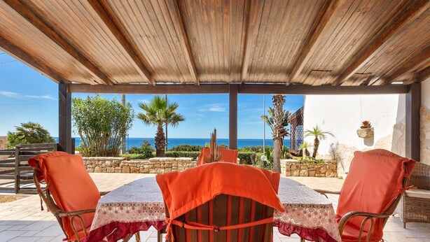 A covered patio with a table and chairs, overlooking a scenic view of the sea and palm trees. - 1907 Villa Alma (Alliste)