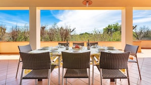An outdoor dining area with a table set for four, surrounded by wicker chairs, under a pergola with a view of the landscape. - 1905 Villa Artas (Tuglie)