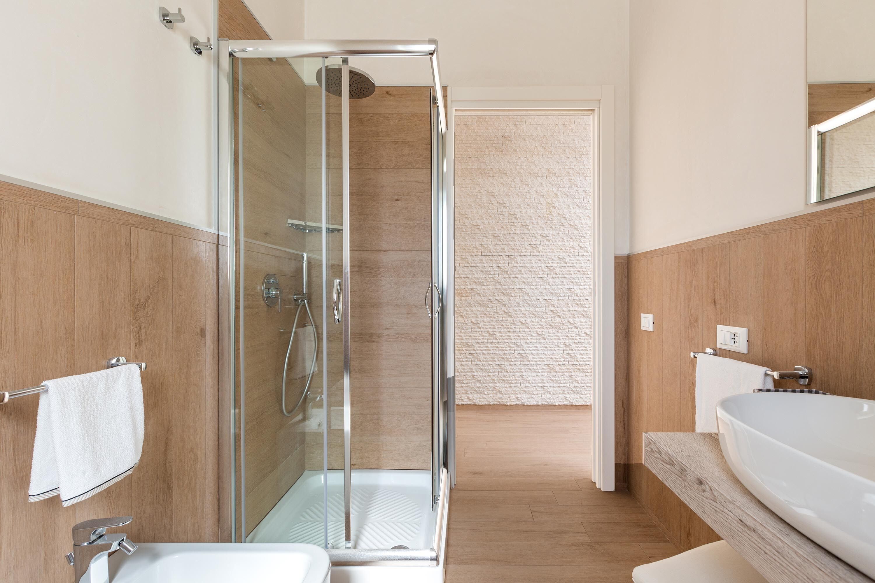 Une salle de bain moderne avec une douche à parois de verre, un grand lavabo blanc et un meuble-lavabo en bois.