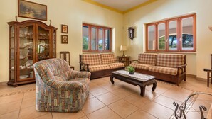 A living room with two sofas, a patterned armchair, a wooden cabinet, and a coffee table. - 1929 Villa Simona (Ugento)