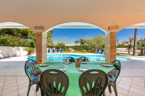 Ein Essbereich im Freien mit Tisch für vier Personen, mit Blick auf einen Swimmingpool und einen Garten.