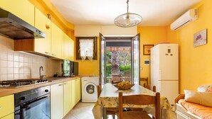 A kitchen with yellow cabinets, a stove, a washing machine, and a dining area with a table and chairs. - 1965 Villino dei Pini (Galatone)