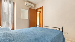 A bedroom with a bed, an air conditioning unit, a door, and a mirror.