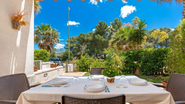 An outdoor dining area with a table set for four, surrounded by wicker chairs, under a clear blue sky.