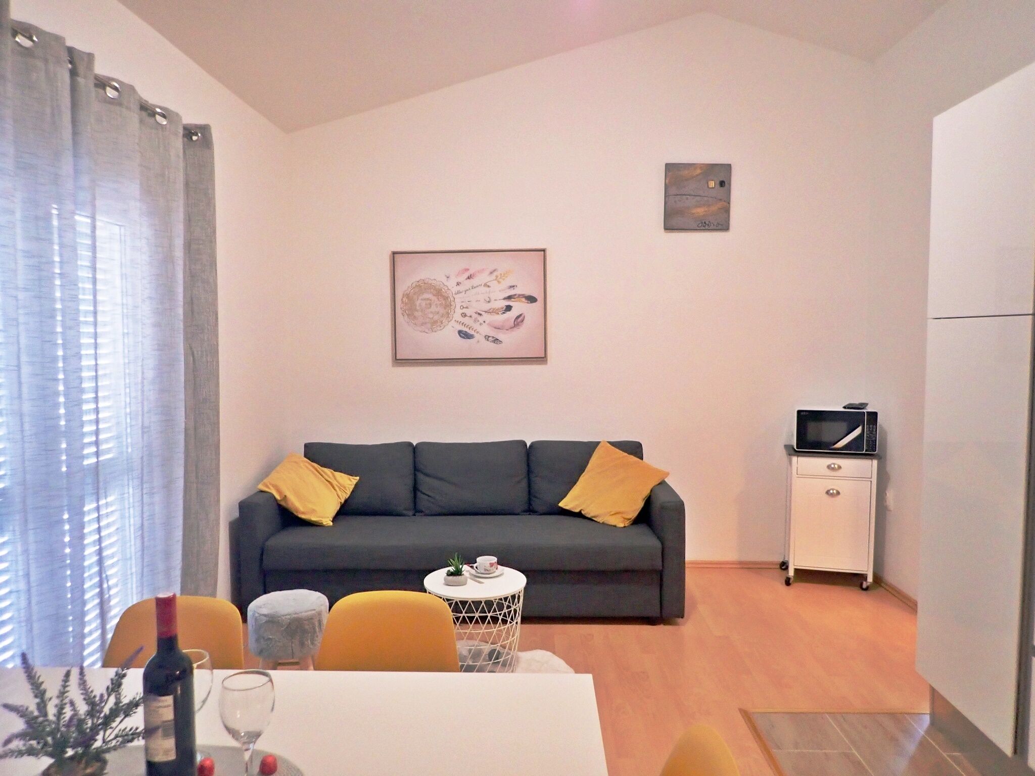 Una sala de estar con un sofá gris, cojines amarillos, una mesita auxiliar blanca y una obra de arte enmarcada en la pared.