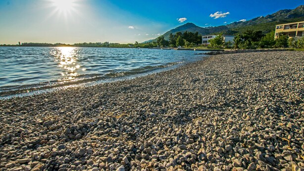 Una spiaggia di ciottoli con una montagna sullo sfondo e un cielo sereno.