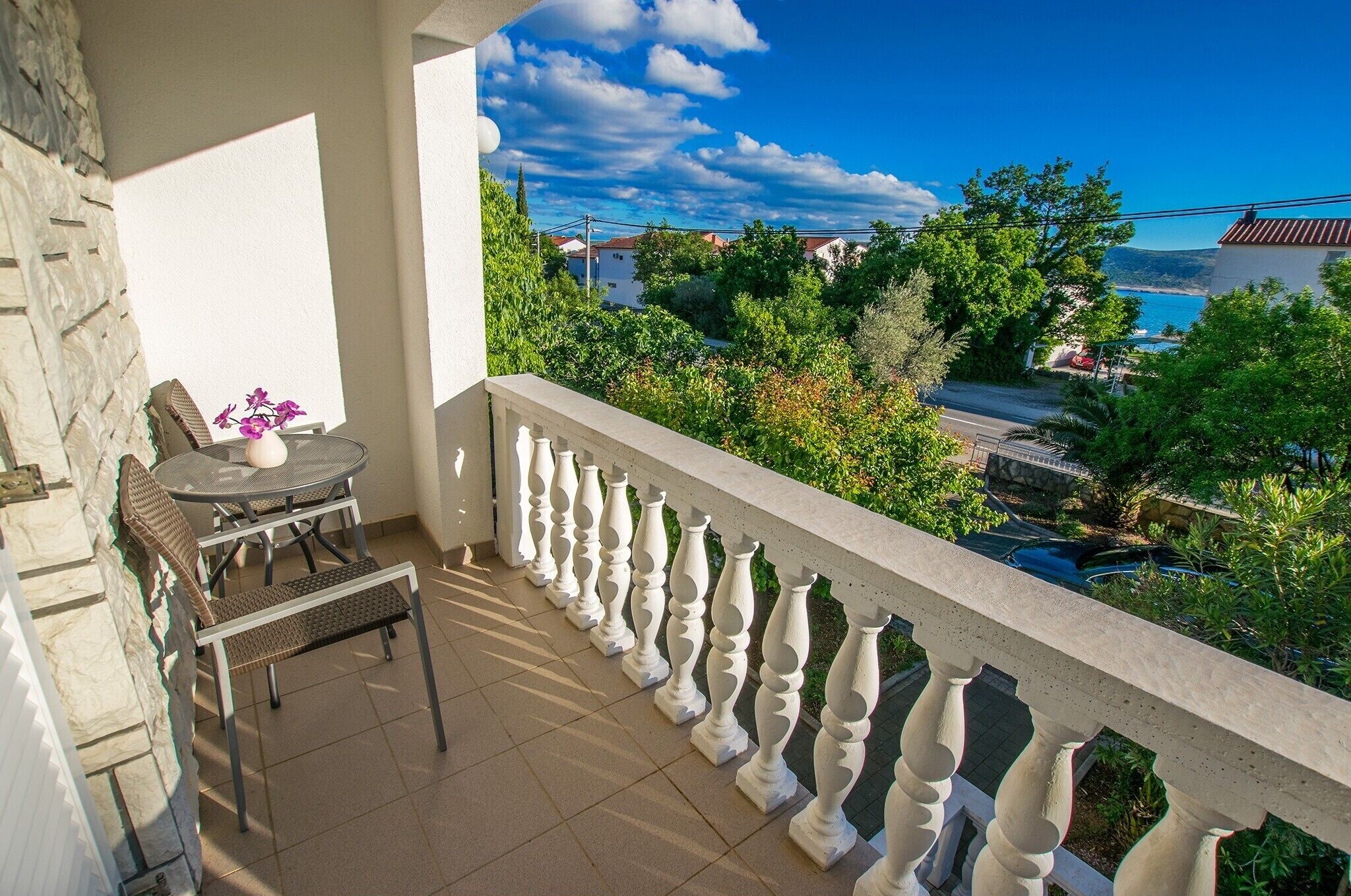 A balcony with a view of a coastal area, a table with chairs, and a vase with flowers.
