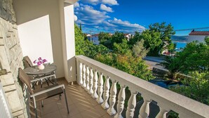 Un balcone con vista sulla costa, un tavolo con sedie e un vaso con fiori.