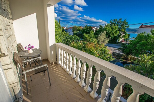 A balcony with a view of a coastal area, a table with chairs, and a vase with flowers.