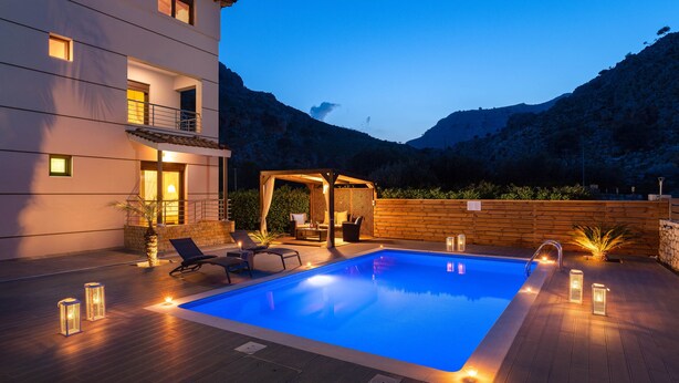 A swimming pool with a wooden deck, lounge chairs, and a pergola.