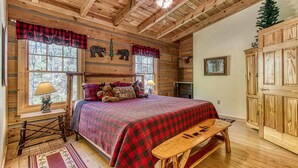 A cozy log cabin bedroom with a large bed, wooden ceiling beams, and a rustic decor theme. - Stream On  -  River Front, $560 FREE tickets each paid day (Sevierville)