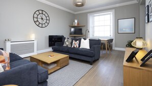 A modern living room with a dark grey sofa, a wooden coffee table, a TV, and a large window providing natural light.
