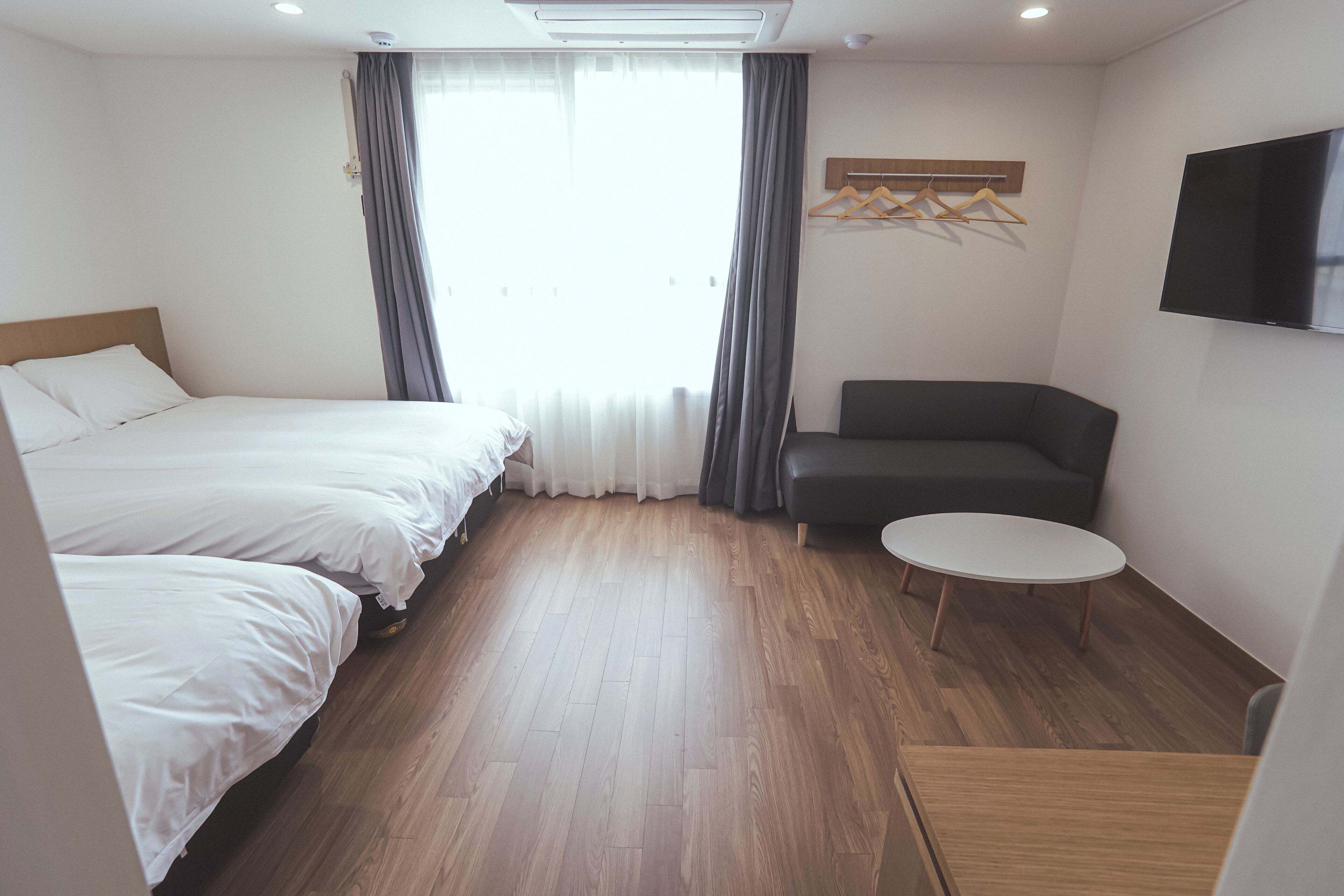 A hotel room with two beds, a sofa, a small table, and a TV on the wall.