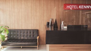 A modern hotel reception area with a wooden wall, a black sofa, and a reception desk.