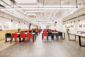 Una cafetería espaciosa con techos altos, conductos expuestos y una combinación de sillas rojas y negras.