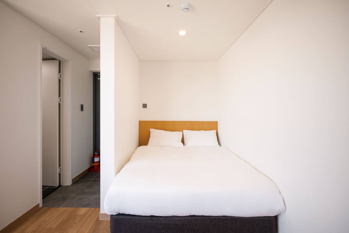 Ett modernt hotellrum med en stor säng, en sänggavel i trä och en stilren, vit färgskala.