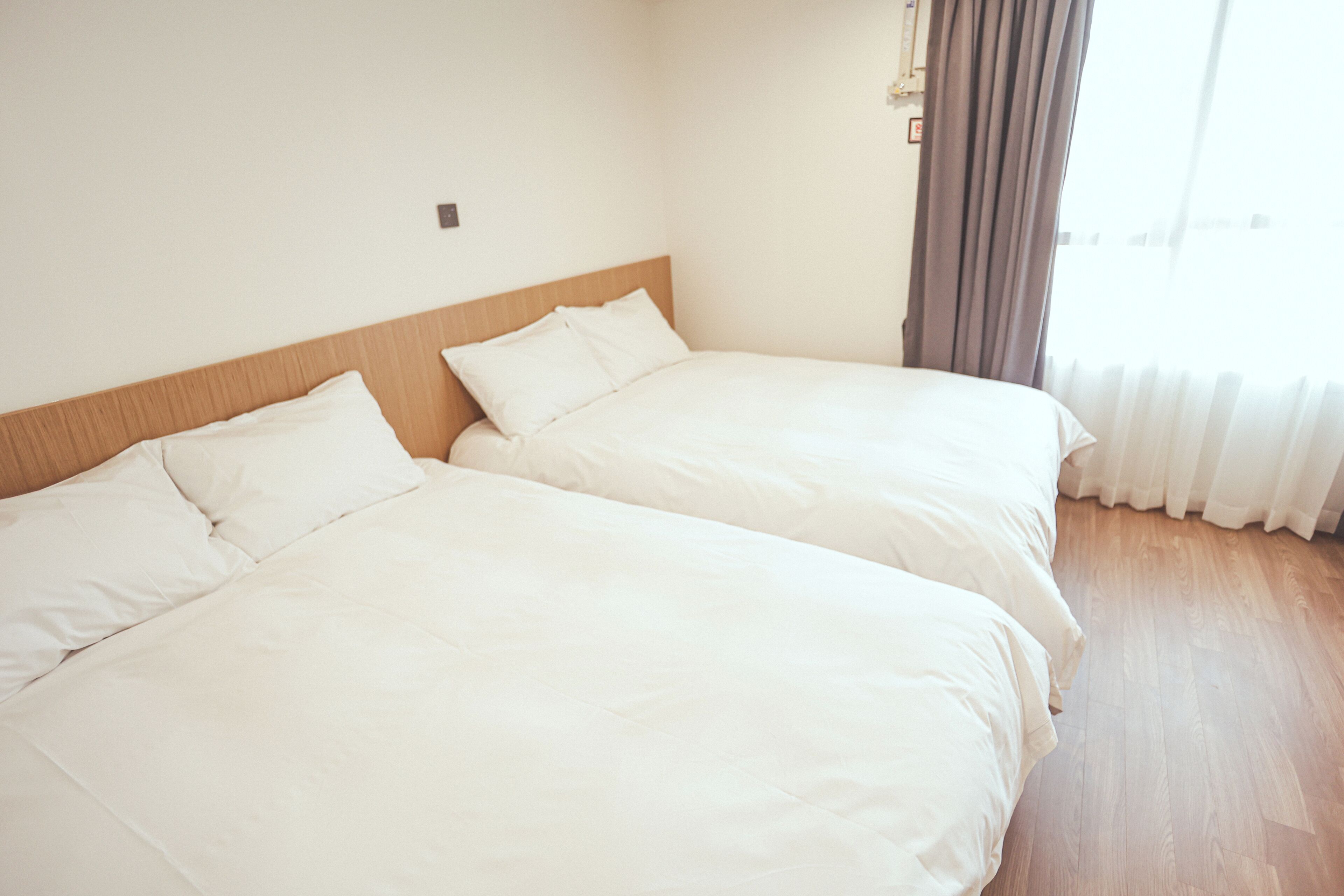 Dos camas individuales en una habitación con suelo de madera y una ventana con cortinas.