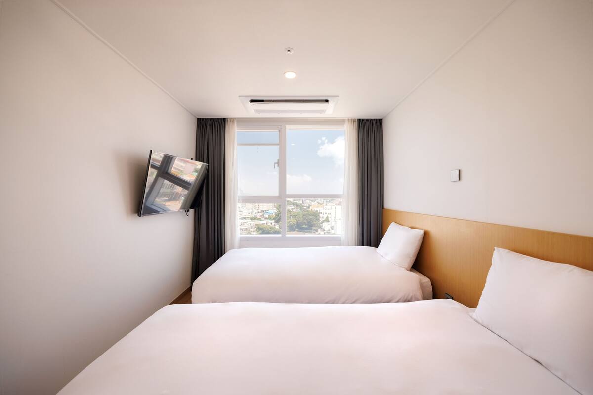 Ett hotellrum med två sängar, en platt-TV som är monterad på väggen och ett fönster med gardiner.