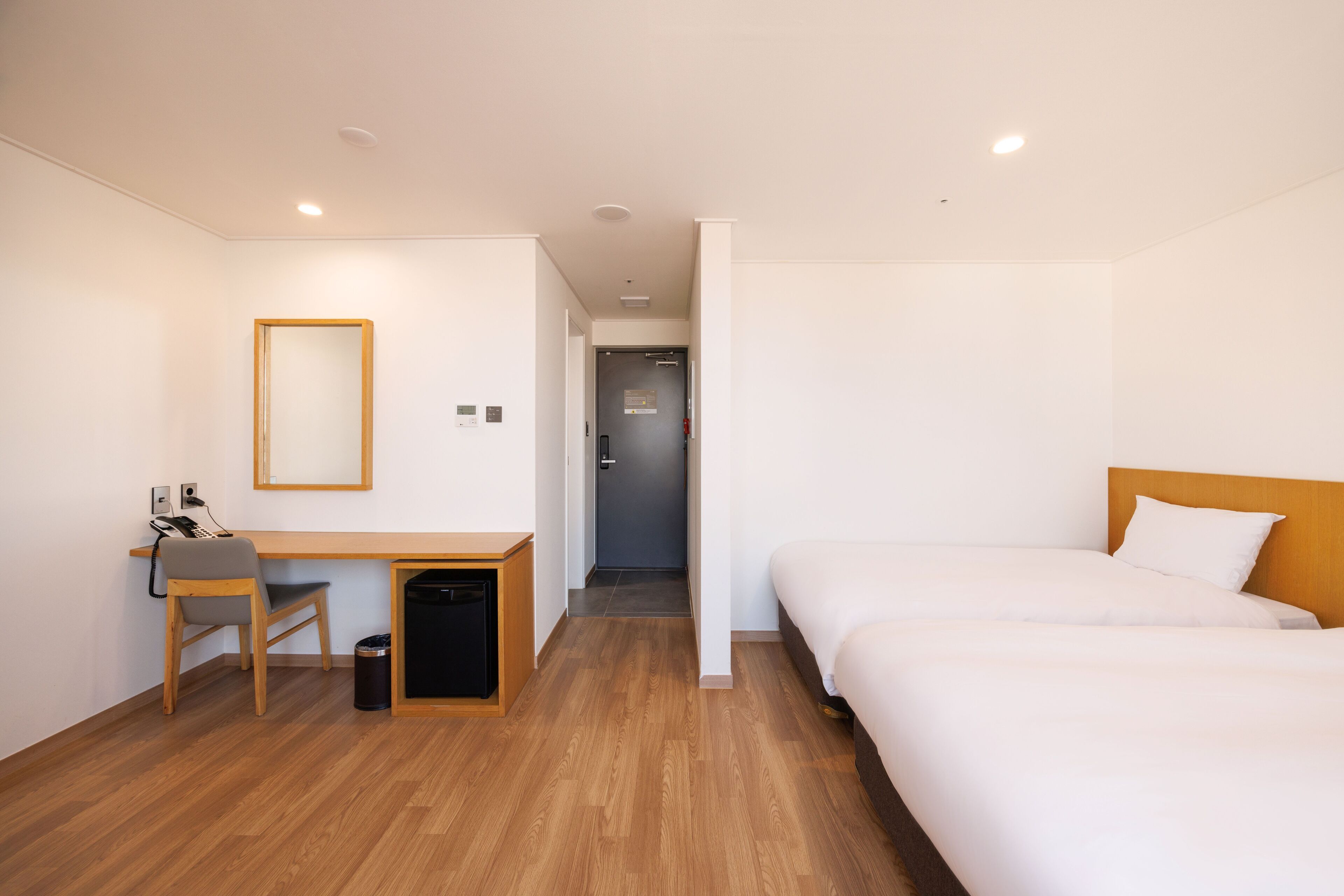 A hotel room with a wooden desk, chair, and two beds.