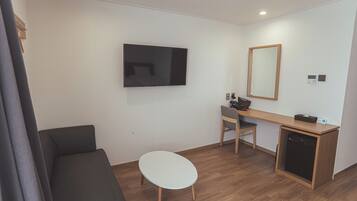 Una habitación moderna con televisión de pantalla plana, un escritorio con silla, una mesita blanca pequeña y un sofá.