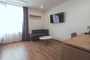 Una habitación moderna con piso de madera, un sofá gris, una pequeña mesa redonda, un televisor montado en la pared y un escritorio de madera.