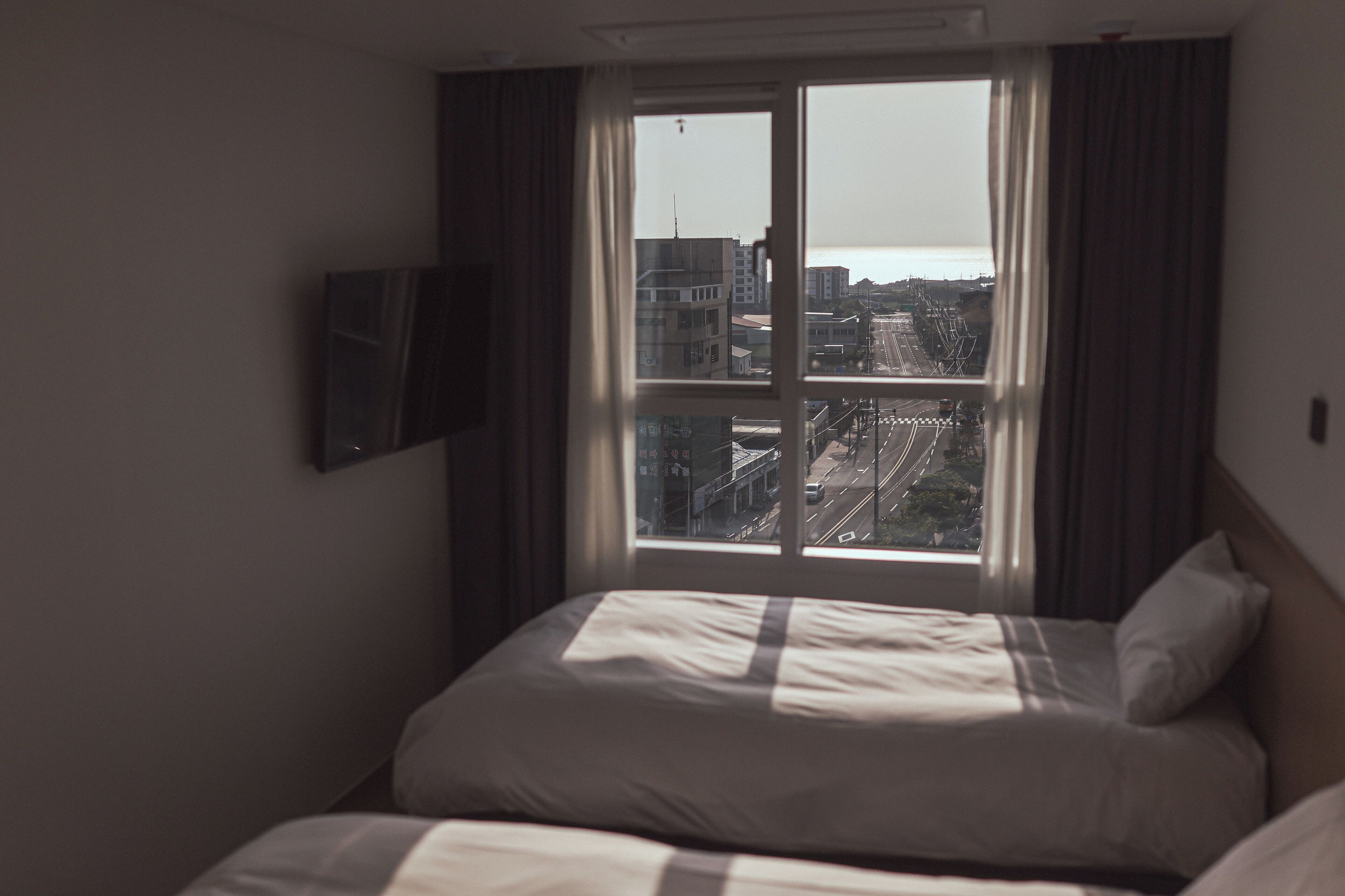 A hotel room with a large window, a bed, and a flat-screen TV mounted on the wall.
