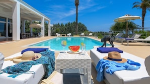 Zona junto a la piscina con sillones de descanso, una mesa con bebidas y vistas a la piscina.