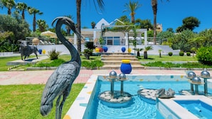 Zona de piscina con una fuente, palmeras y una estatua de un ave.