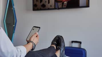 Una persona sentada en una cama con una maleta, sosteniendo un teléfono inteligente.
