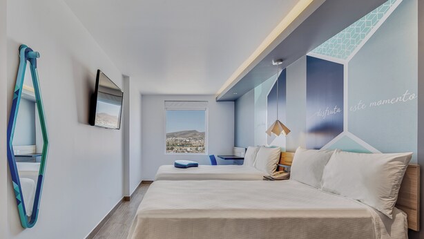 Ein modernes Hotelzimmer mit einem großen Bett, einem Schreibtisch, einem Sessel und Blick auf die Stadt.