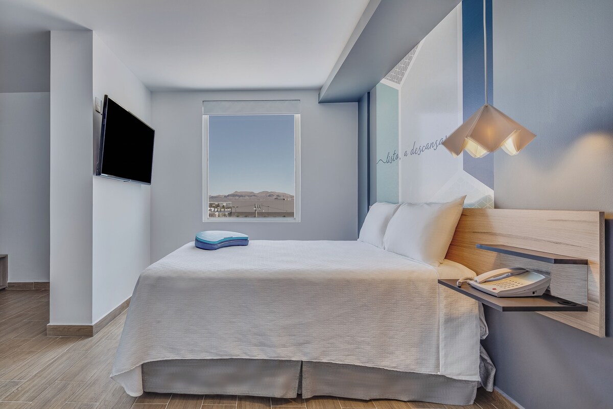 Een moderne slaapkamer met een bed, een wandtelevisie, een bedtafeltelefoon en uitzicht op het landschap door een raam.