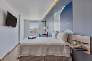 Moderni hotellihuone, jossa on sänky, työpöytä, tuoli, puhelin ja televisio.
