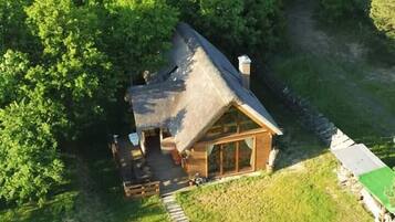 A wooden cabin with a thatched roof, surrounded by dense green trees.