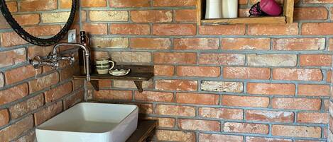 A bathroom with a white sink, a toilet, and a shelf with toiletries.