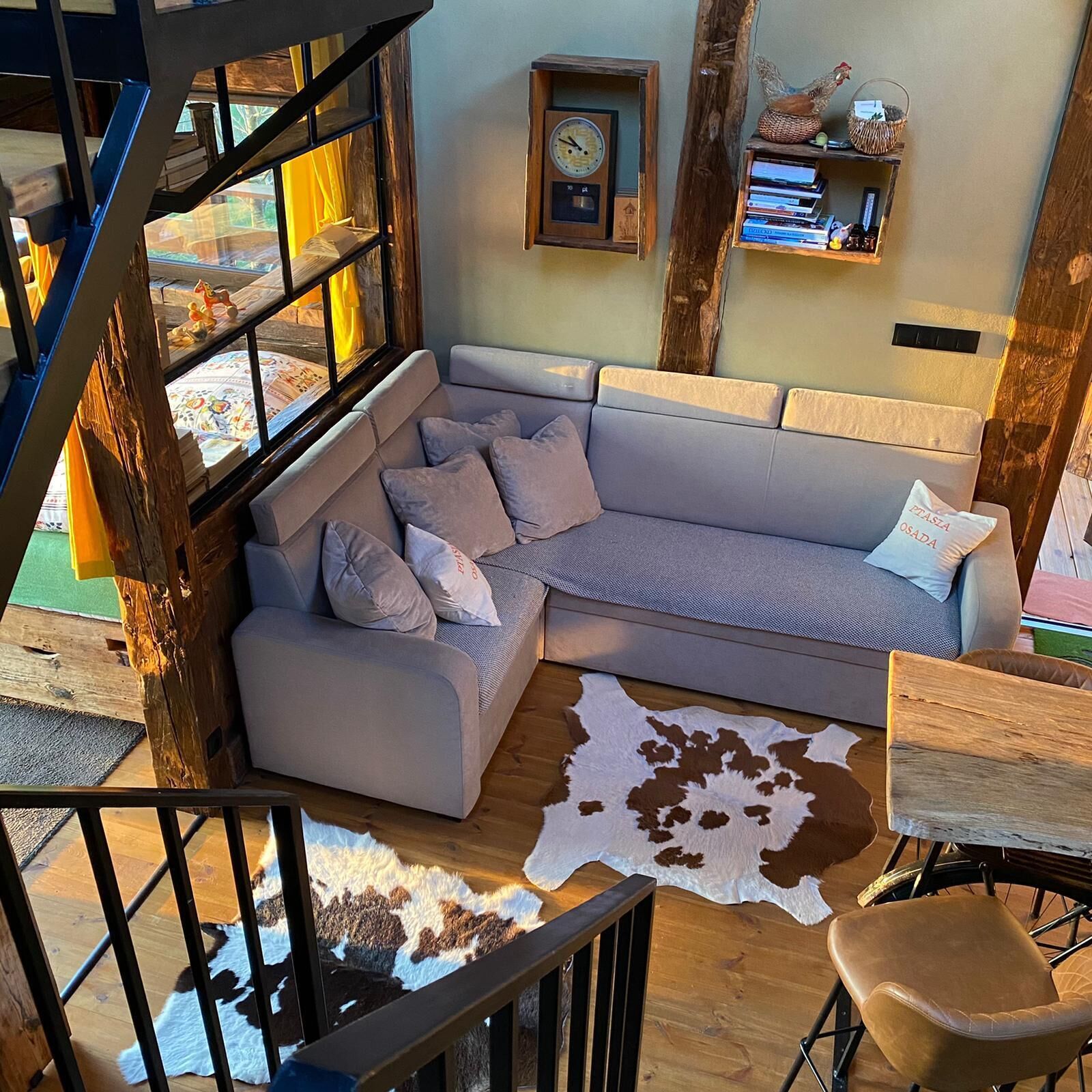 Una sala de estar moderna con un sofá seccional, una escalera de madera, un tapete de cuero de vaca y decoración rústica en la pared.