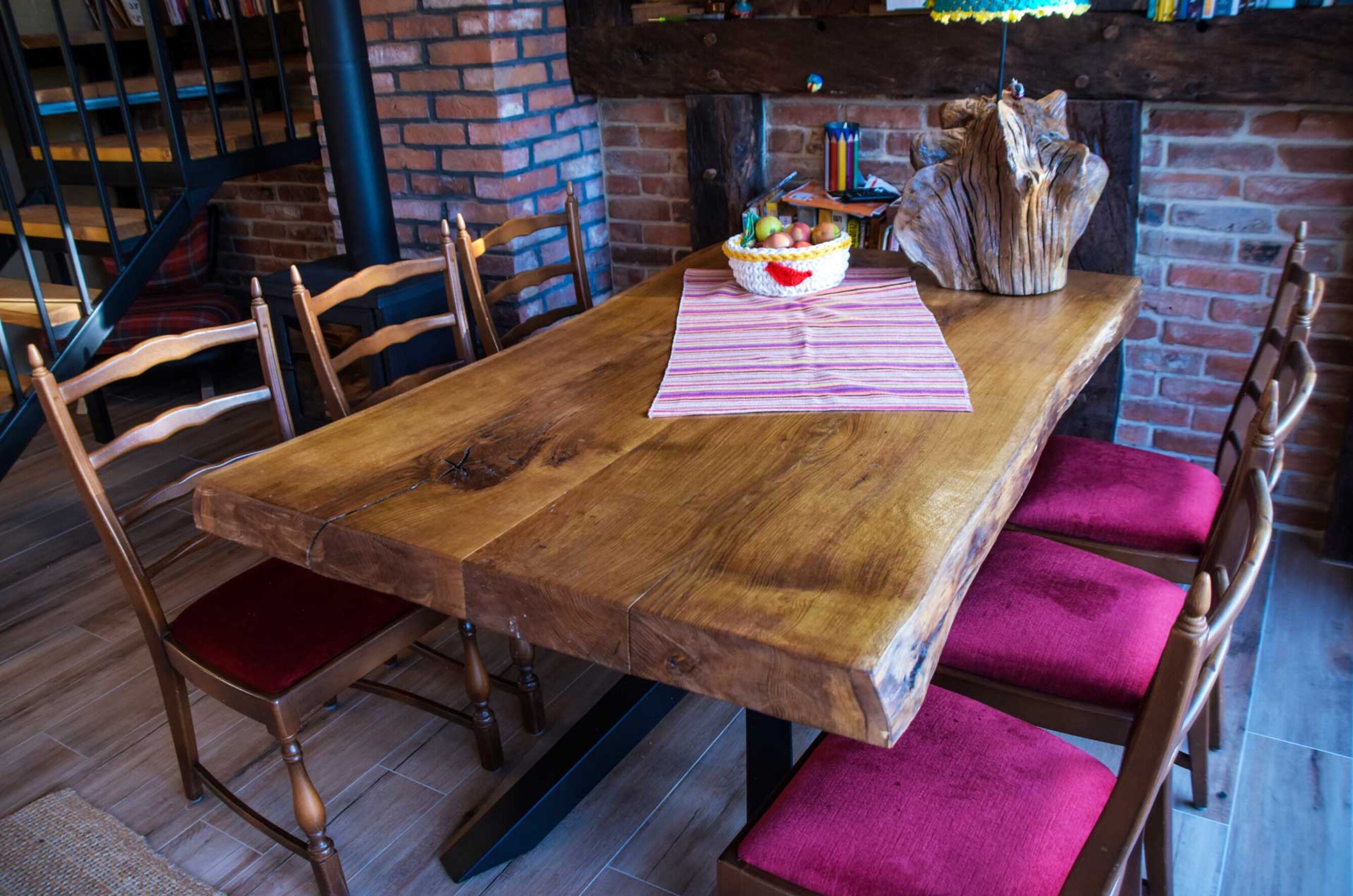 A wooden dining table with a basket of fruit, a striped placemat, and a rustic vase.