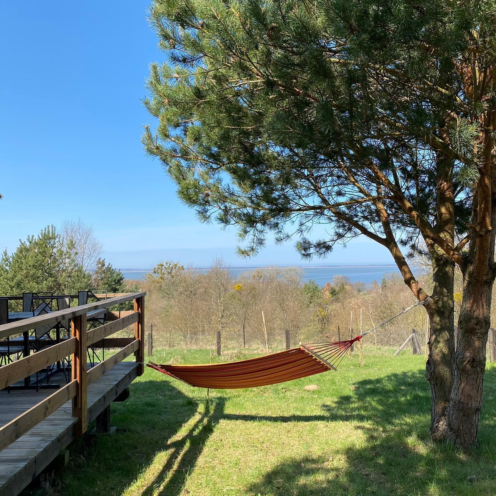 A hammock tied to a tree, a wooden deck, and a view of the landscape.