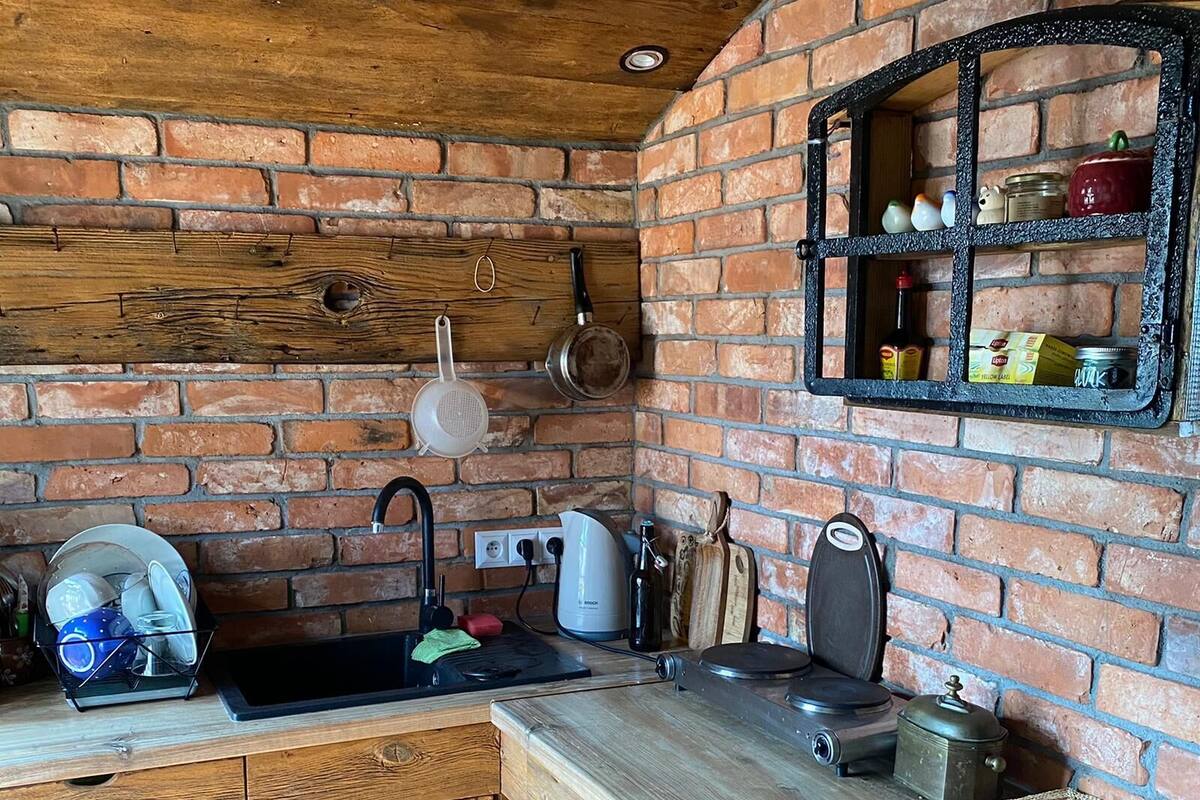 A rustic kitchen with a brick wall, wooden cabinets, and a built-in shelf with kitchen items.