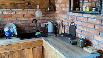 A rustic kitchen with a brick wall, wooden cabinets, and a built-in shelf with kitchen items.
