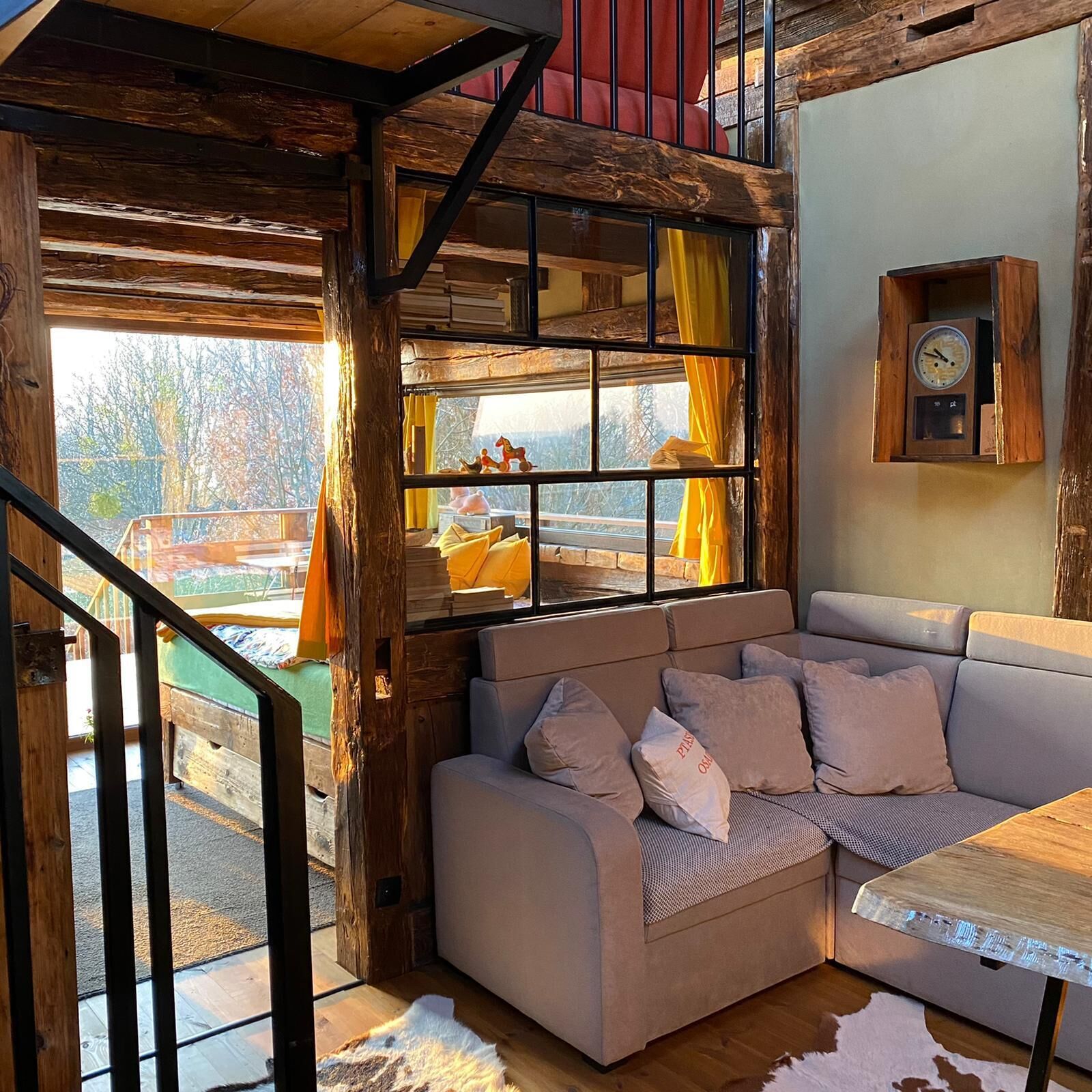 Interior acogedor de una cabaña con escalera de madera, sofá con cojines, chimenea y estante de madera rústica.