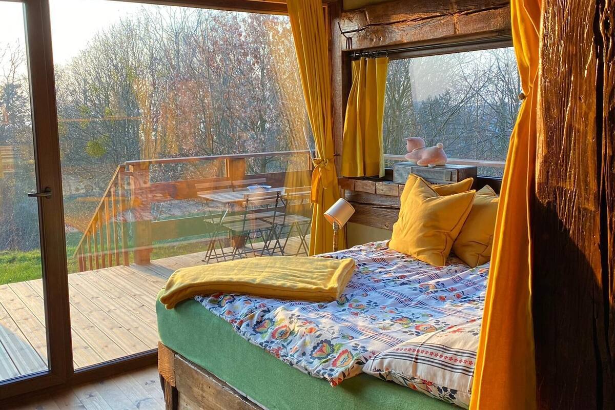 A bedroom with a wooden headboard, a bed with a floral bedspread, yellow pillows, and a view of the outdoors through a glass door.