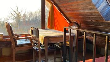 Ein gemütliches Schlafzimmer unter dem Dach mit schrägen Wänden, Holzbalken und einem großen Fenster. Ein Holztisch mit Stühlen und ein rotes Sofa sind ebenfalls vorhanden.