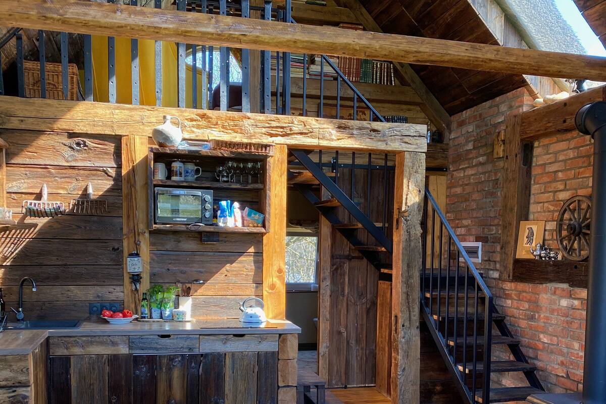 A rustic interior with a wooden staircase, a kitchen area with a microwave, and a cozy seating area with a couch and pillows.