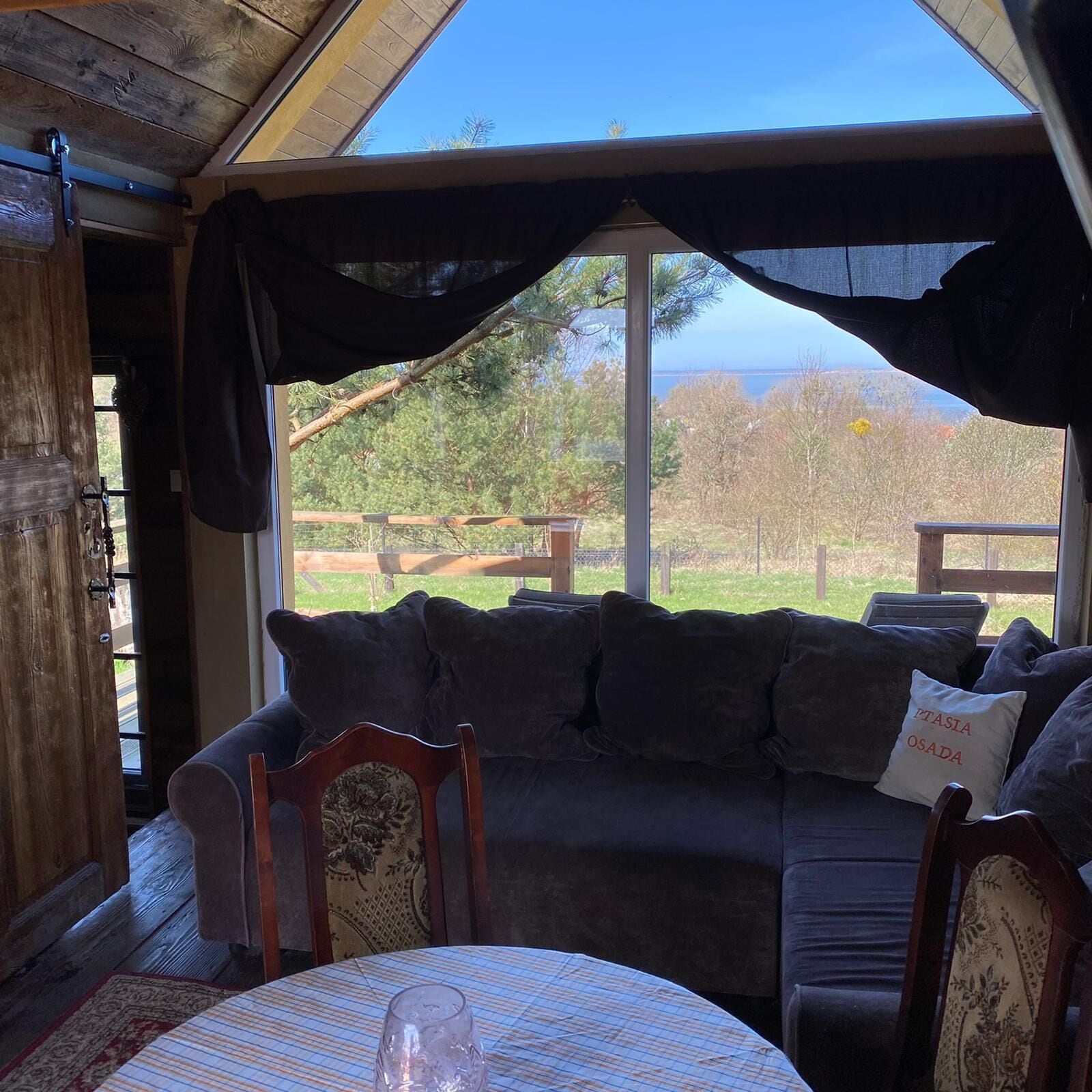 Um quarto acolhedor com uma janela grande, teto de madeira e sofá escuro com almofada rotulada "PTASIA OSADA".