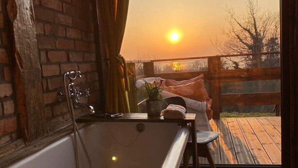 Un baño con bañera, terraza de madera y vistas al atardecer.